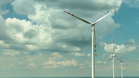 Aerial-footage-featuring-a-row-of-wind-turbines-set-against-a-sky-filled-with-dynamic,-fluffy-clouds