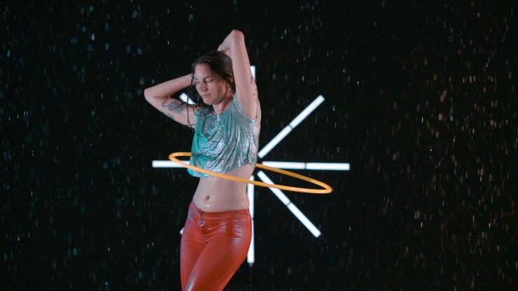 Bella donna che pratica hula hoop balla elegantemente con l'hula hoop in uno studio bagnato, al rallentatore.