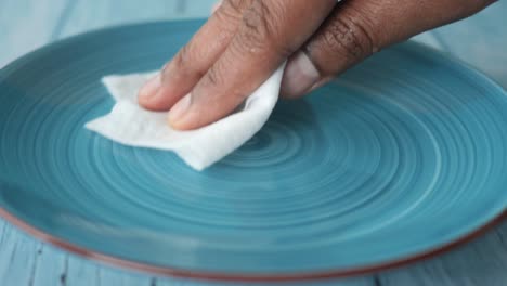 a hand cleaning a blue plate with a paper towel