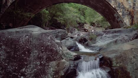 una cascata che scorre sul bordo delle rocce sotto un vecchio ponte