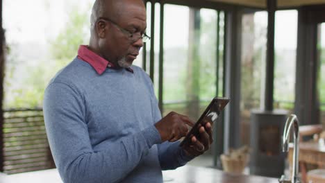 African-american-senior-man-at-counter-in-kitchen-using-tablet,-looking-away