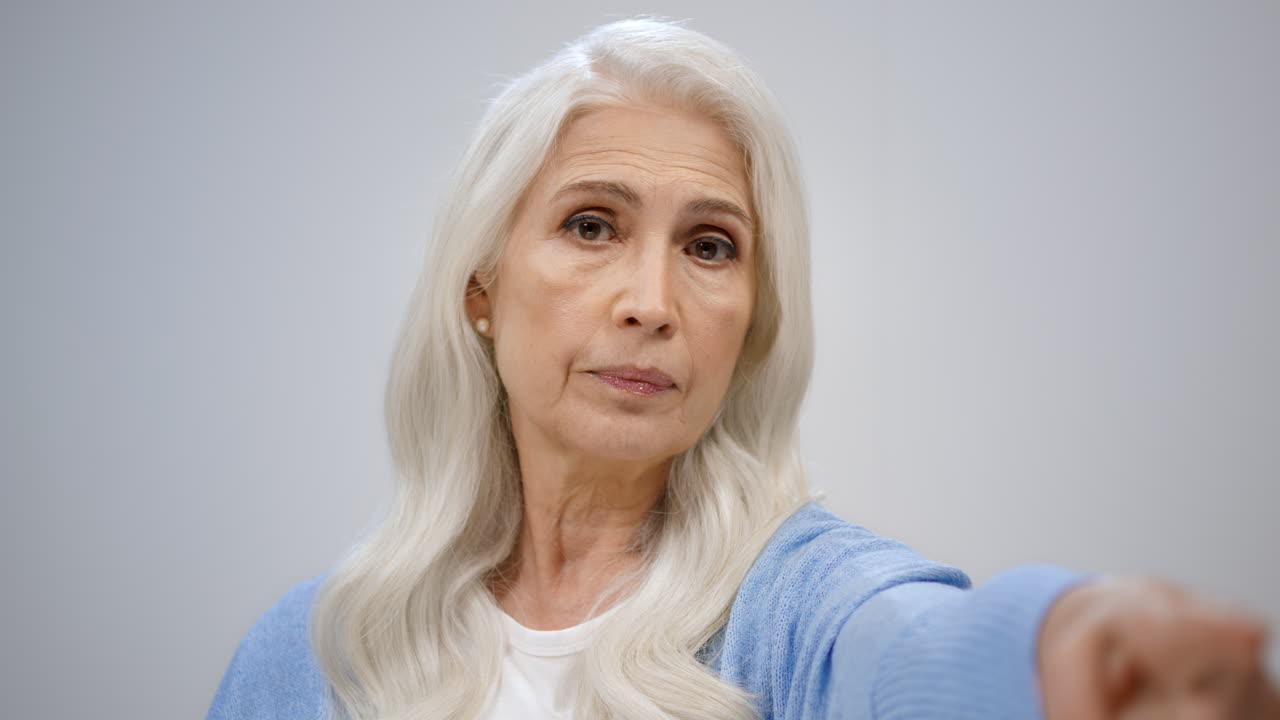 Mature woman pointing to camera indoors. Serious lady looking strict in studio.