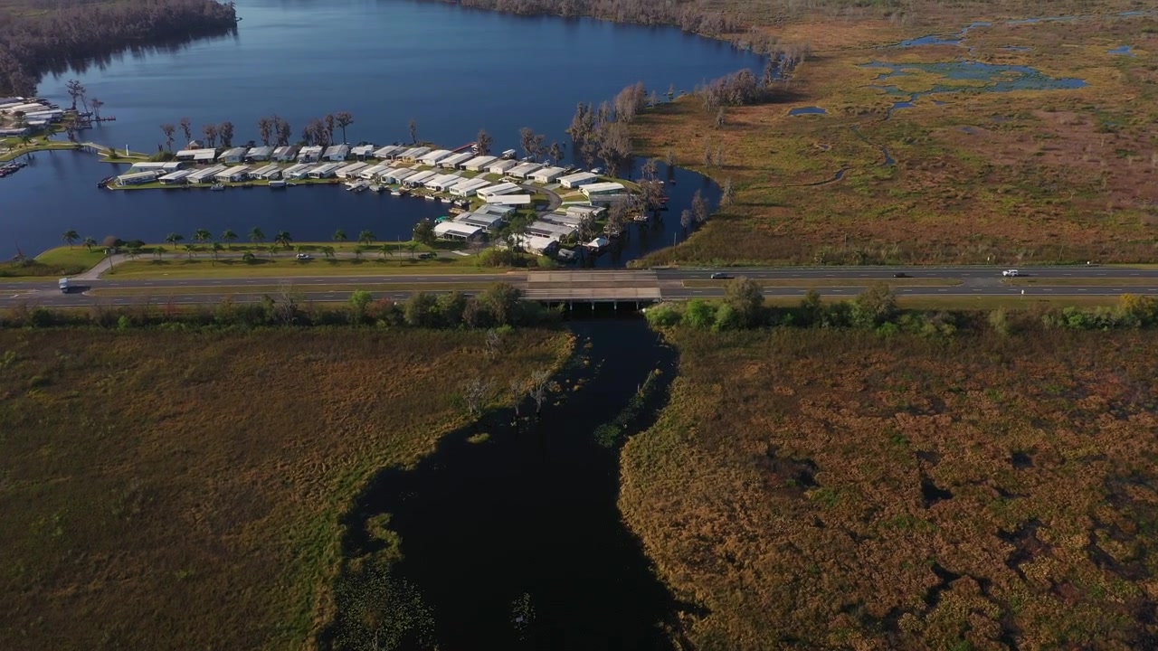 Luftfoto af Highway 50, der krydser Palatlakaha-floden i Clermont, Florida, med et mobilhjemssamfund ved søen og vådområder, der strækker sig langs Clermont Chain of Lakes