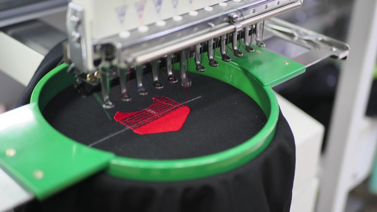 Macchina da ricamo industriale che ricama un disegno rosso su tessuto nero