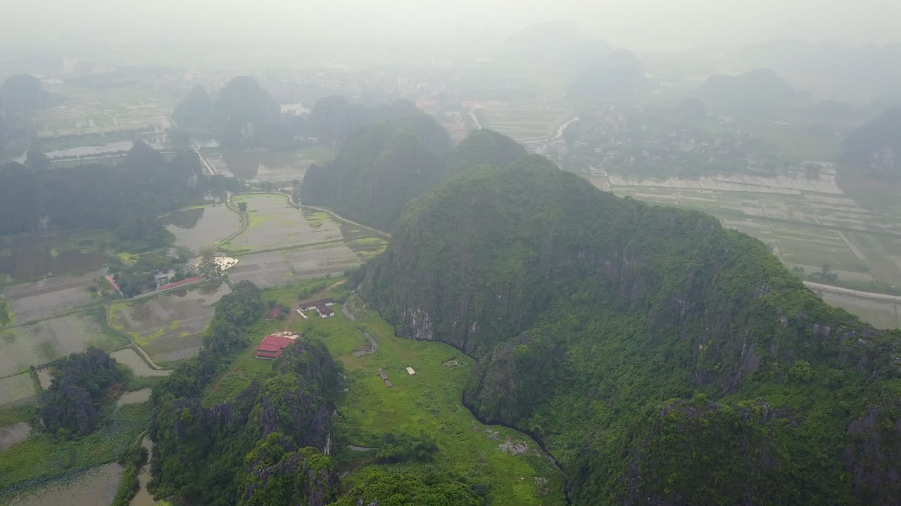 An aerial perspective captures the serene beauty of a rainy and cloudy day in Ninh Binh, Vietnam, showcasing the lush green rice fields nestled amongst the region's iconic karst formations