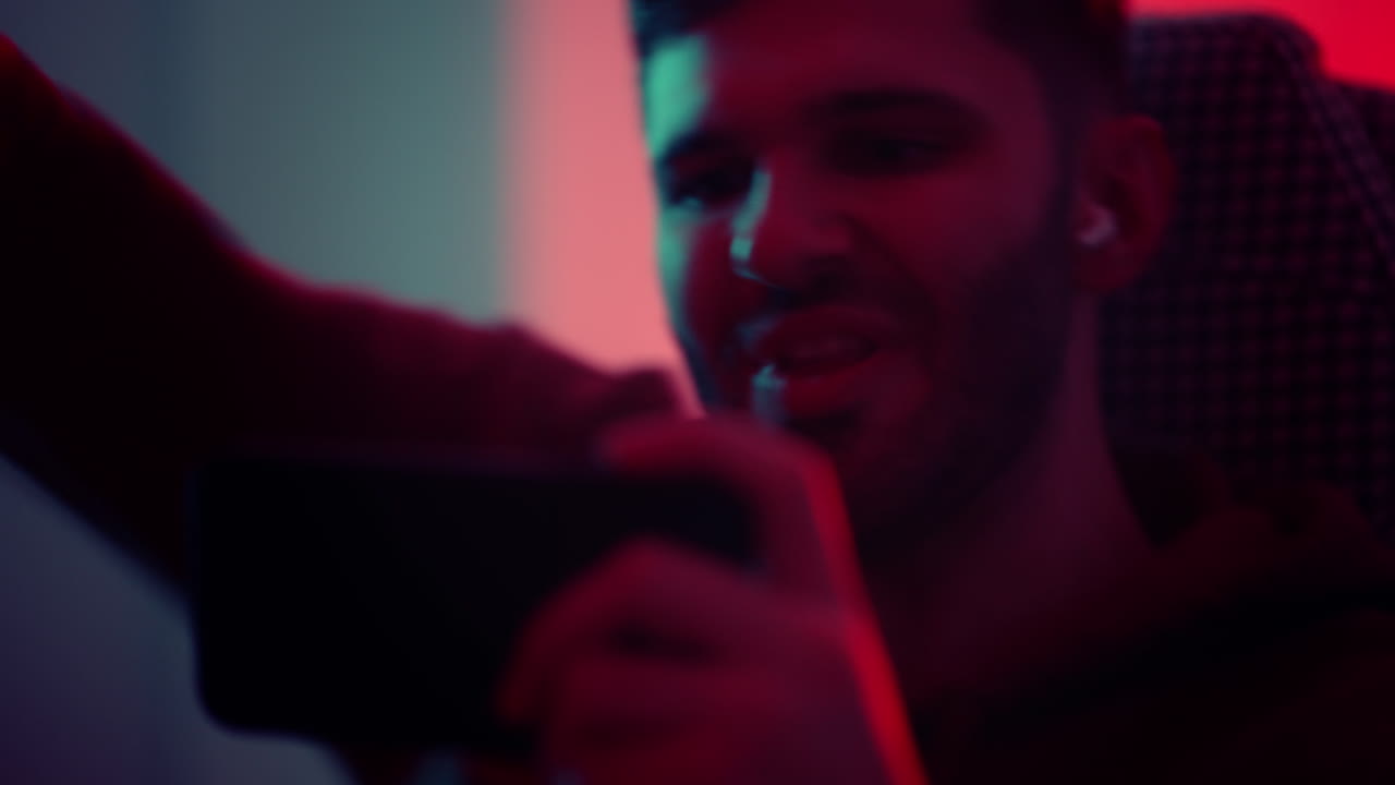 A young man with glasses a professional gamer on a mobile phone plays games and emotionally rejoices in the victory. Emotional young man playing mobile games in a neon light. High quality 4k footage