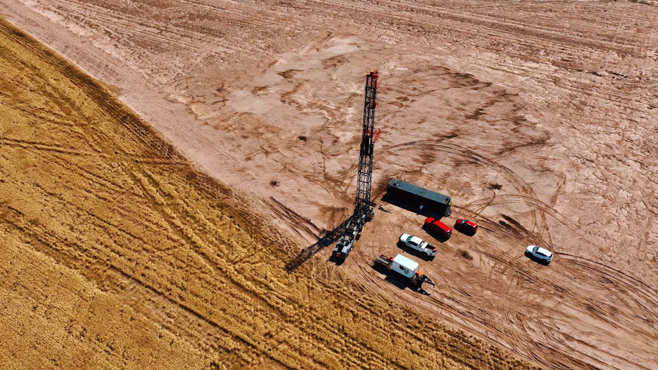 Oil production site near the wheat field away from the big cities. Few cars stand at the derrick for drilling oil. Aerial view.