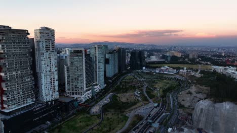 Aerial-view-away-from-the-Parque-La-Mexicana-park,-dusk-in-Santa-Fe,-Mexico---pull-back,-drone-shot