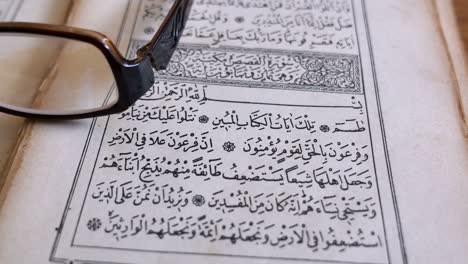 a quran lying on a table with reading glasses on it, the shot moves from left to right