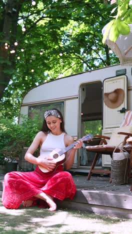 teenage girl playing ukulele outdoors in a garden near a campervan