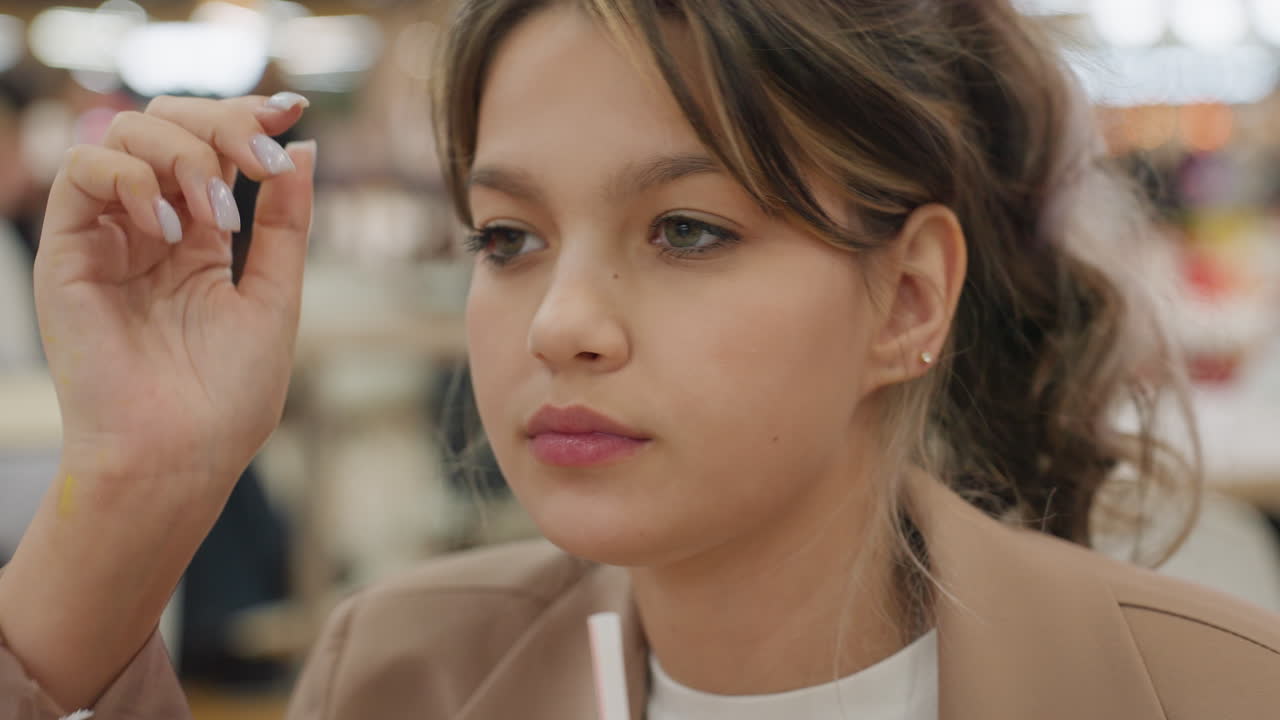 Joven tranquilo saboreando su comida, adolescente pensativo relajándose en un patio de comidas animado, joven caucásico reflexivo descansando plácidamente después de comer rodeado de un ambiente ajetreado