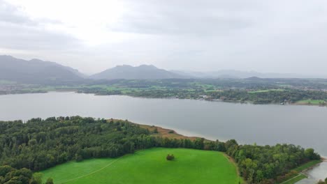 Chiemsee,-Bavaria,-Germany---A-Freshwater-Lake-Encircled-by-Vibrant-Green-Landscapes,-Framed-Against-a-Backdrop-of-Majestic-Mountains---Aerial-Pan-Right