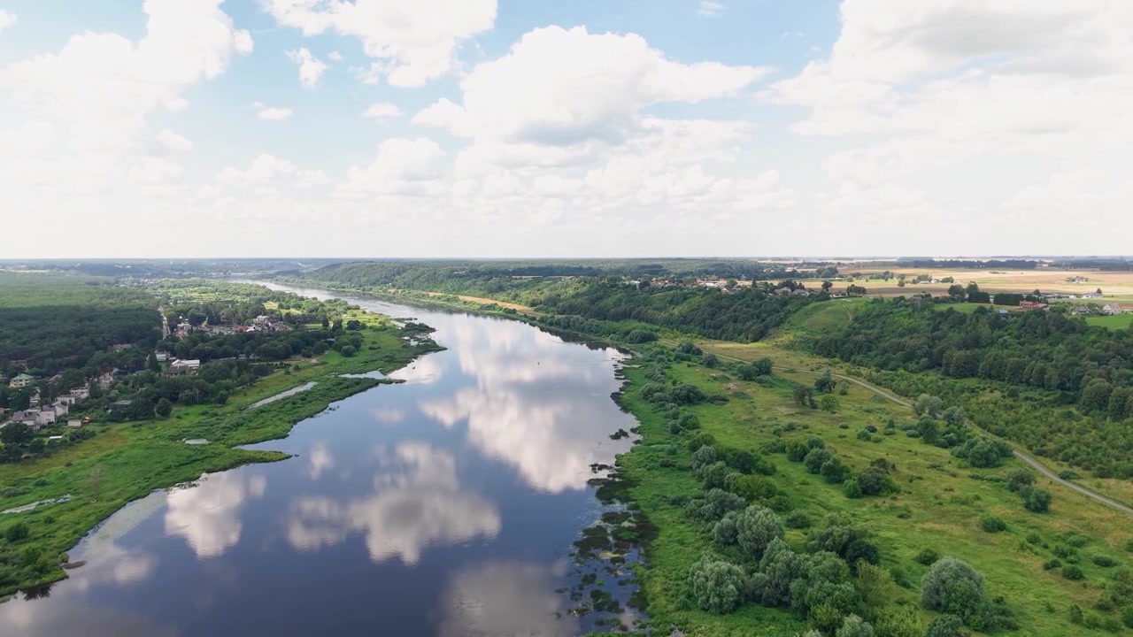 Ohromující video z dronu zachycuje klidnou řeku vinoucí se skrze živá zelená pole, odrážející dramatické mraky pod modrou oblohou. Panorama odhaluje nedotčenou přírodu, letní světlo a klidnou atmosféru