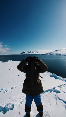 a person observing a vast snowy and icy landscape with binoculars