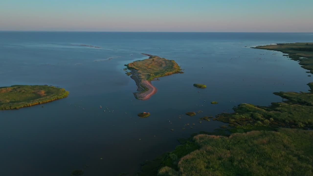 Drone shot of green island islet in summer, moving backwards away from the sea revealing green coastline