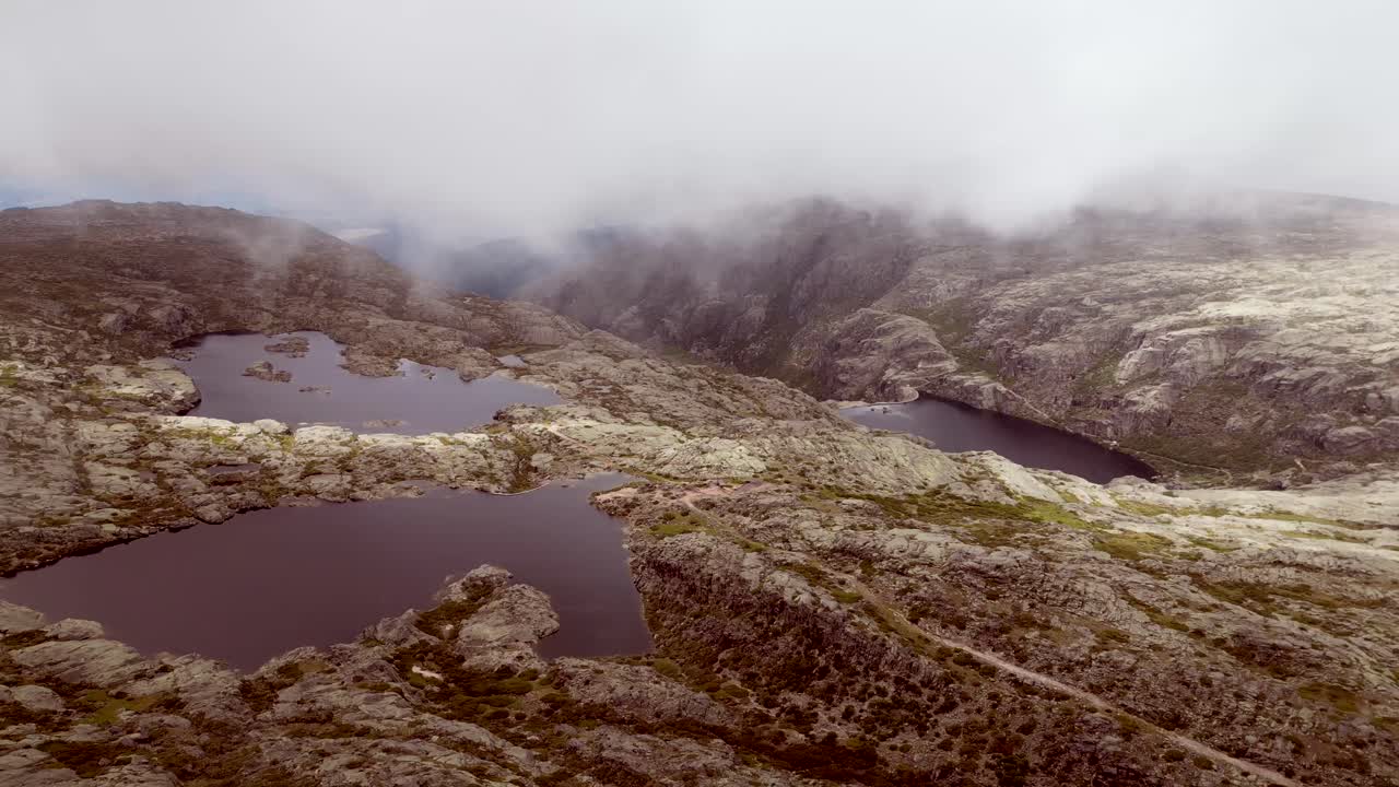 Using a drone, slow-motion footage captures the lake perched atop the highest point of Serra de Estrella, as clouds gently obscure the mountain