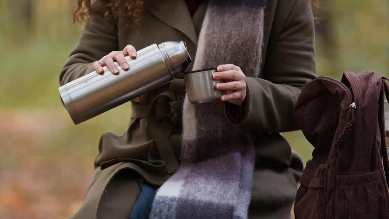Woman pouring hot drink from thermos in park