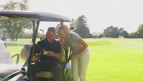 mature couple playing round on golf together sitting in buggy with score card