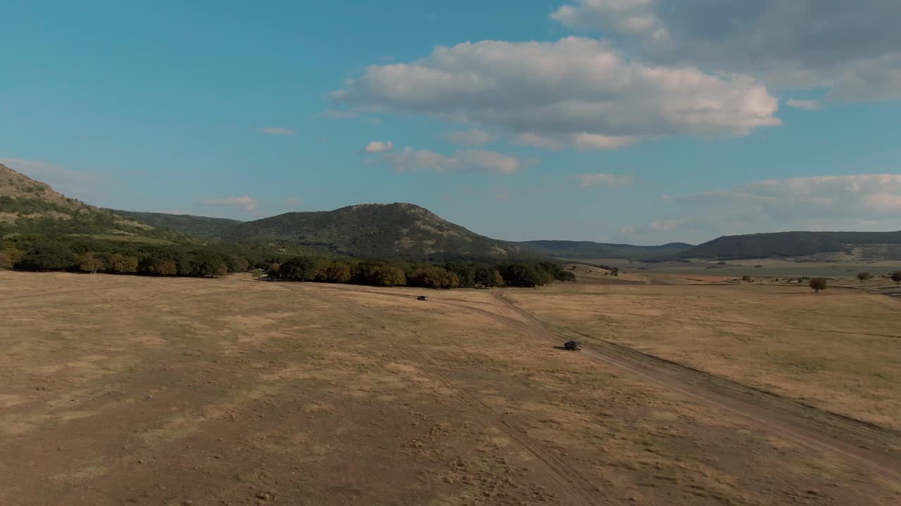 Toma de seguimiento con dron de todoterrenos distantes conduciendo por una carretera rural, en un día soleado y despejado.