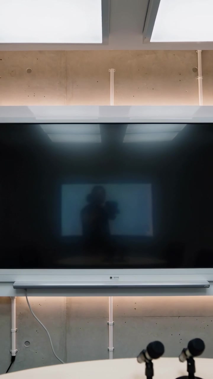 Video verticale: Telecamera in movimento che mostra un telefono riflesso, tecnico che posiziona apparecchiature AV e microfoni nella sala riunioni.