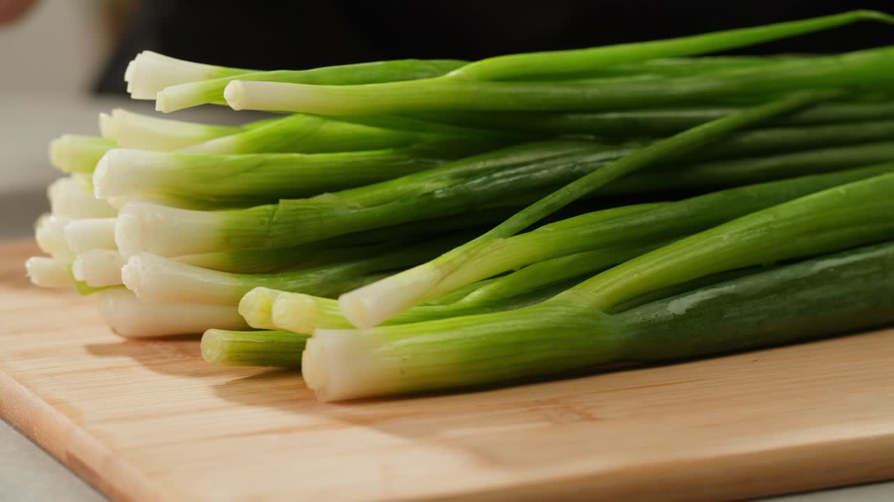 Cutting fresh green onions on a cutting board, close up chef cooking green vegan salad.