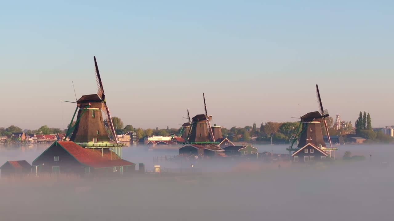 Vista aerea di mulini storici e di un tranquillo corso d'acqua velati dalla nebbia, in Olanda.