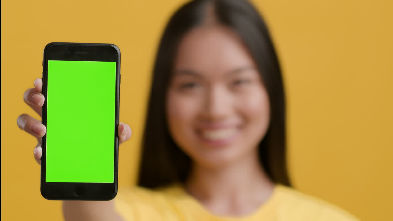 Smiling woman showing smartphone with green screen for content display