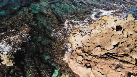 low aerial drone shot exploring over a mix of rocky shore of majorca and the clear blue water mediterranean