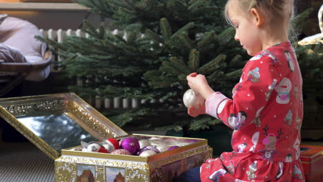 niño pequeño con pijama rojo poniendo adornos en un árbol de navidad