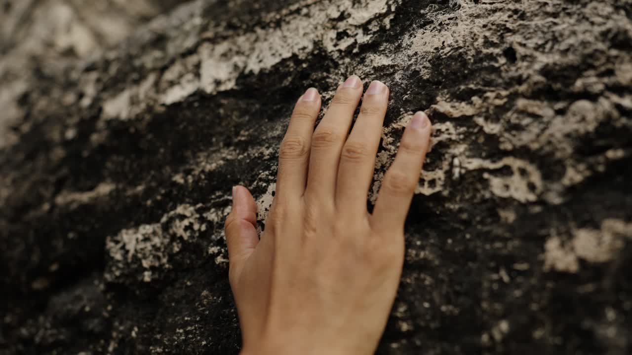 A close-up of a human Mayan hand gently placed on the aged stone wall of a Mayan structure in Tikal, evoking connection and reverence.