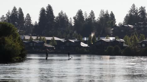 Kalter-Morgenfluss-Mit-Zwei-Silhouettierten-Paddelboardern-Und-Bäumen