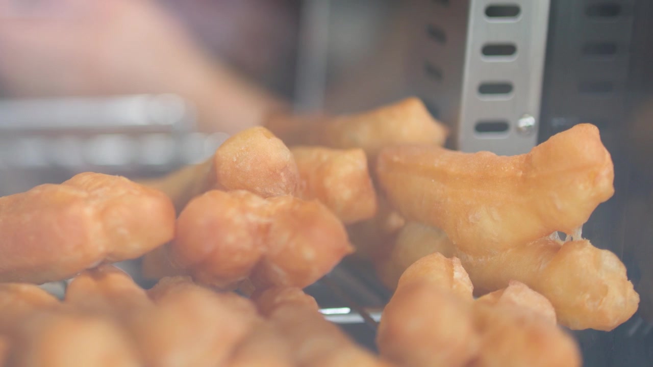 Primo piano di bastoncini di pasta fritta asiatica croccanti che riposano su una griglia metallica all'interno di una vetrina