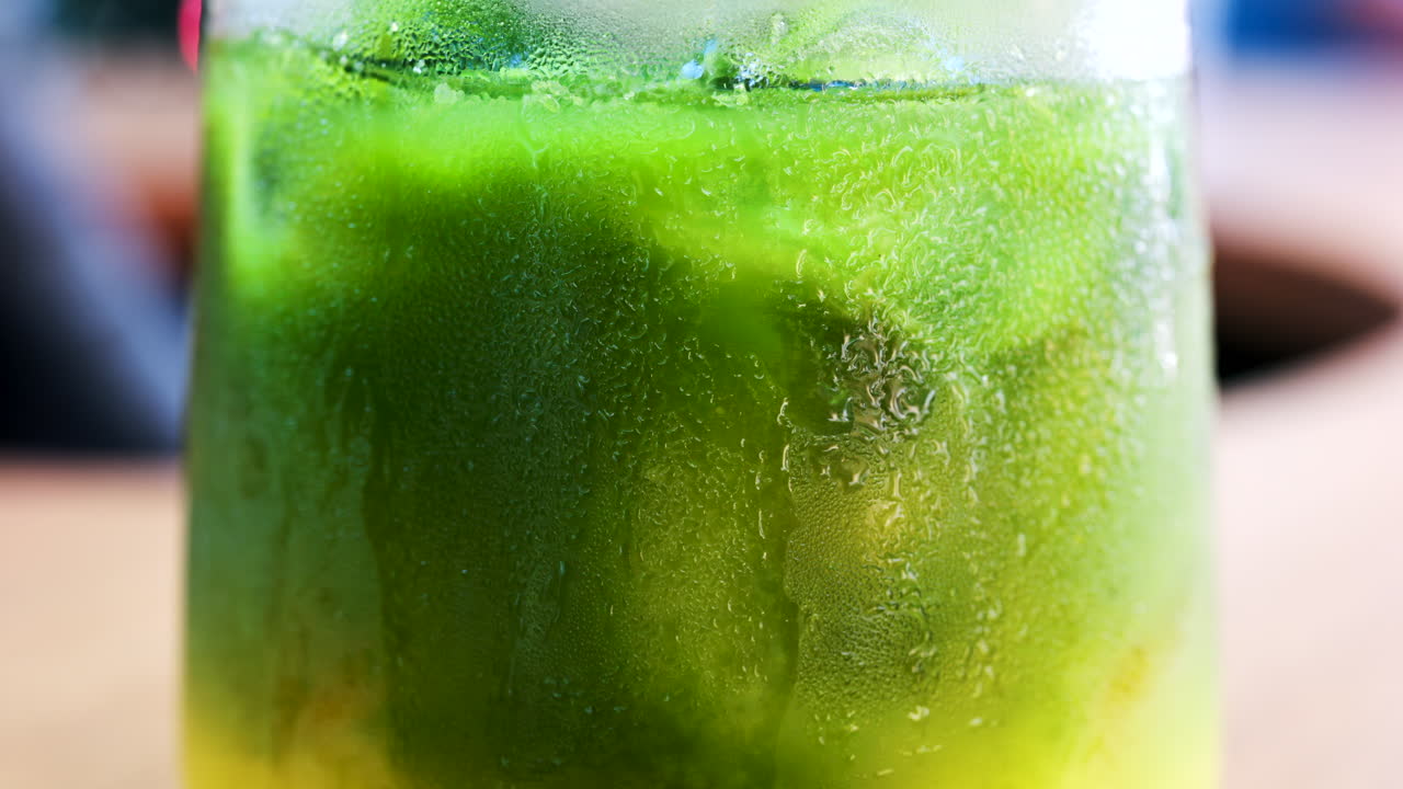 Close up of a glass of an iced orange juice matcha on a table at a cafe