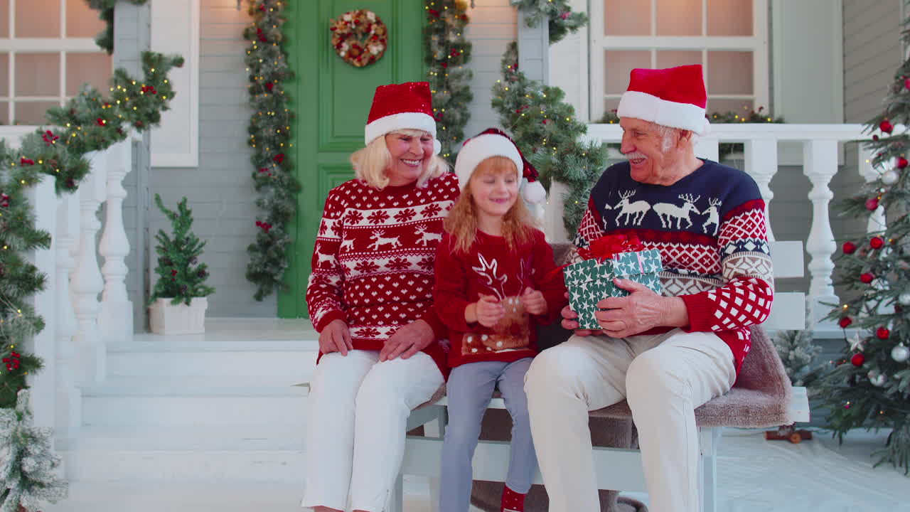 nieta regalando caja de regalo de navidad a abuelos felices y asombrados en casa, celebrando