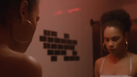 beautiful girl putting lipstick on while looking at mirror in a bar bathroom