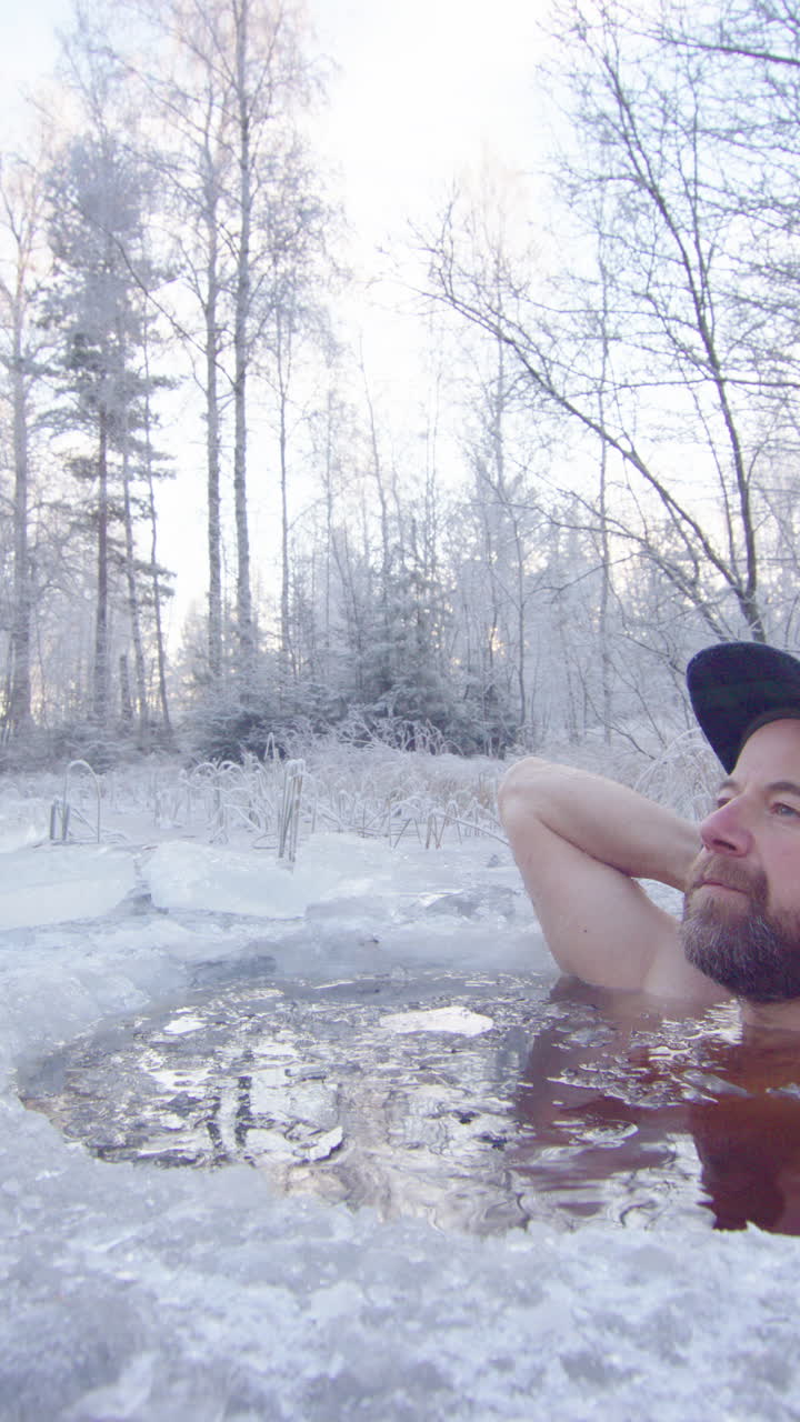 A very relaxed ice bather enjoys a cold bath in a frozen Swedish lake, vertical