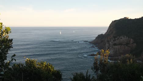 wo catamarans sail calmly toward knysna heads during blue hour. the sun is setting, casting soft light on a peaceful, beautiful day. filmed in stunning 4k with a static shot