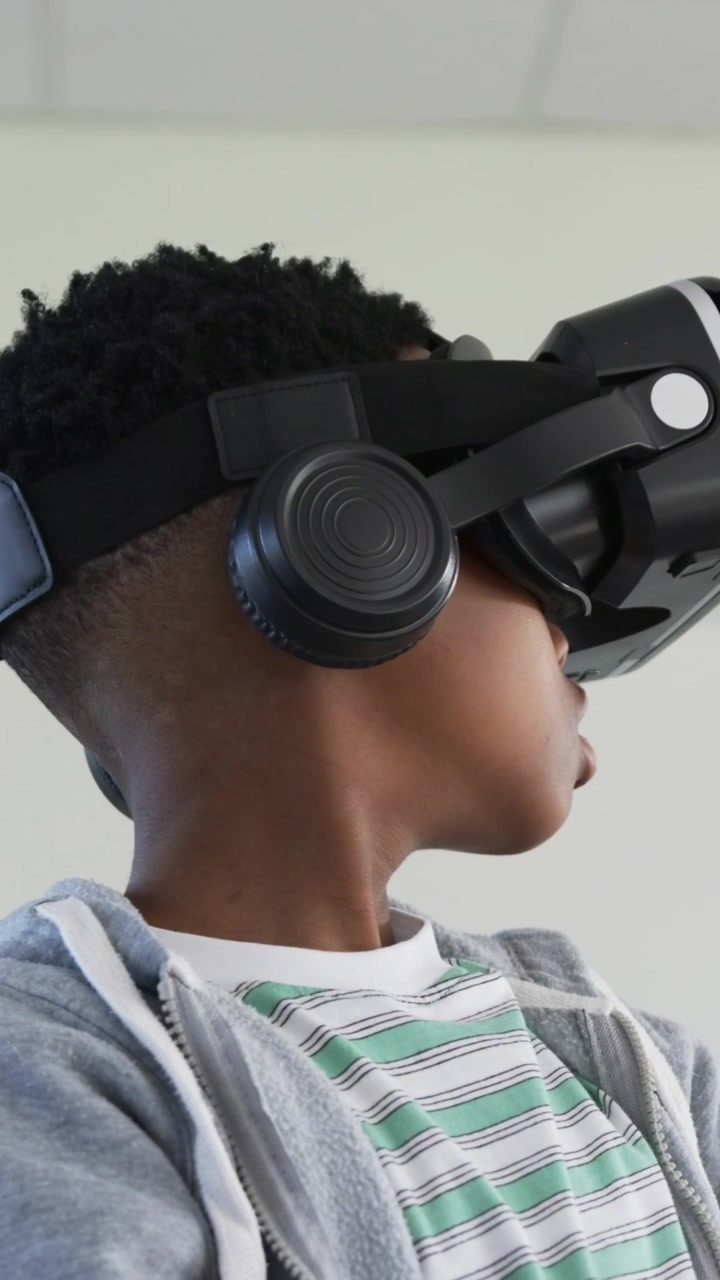Vertikal video: Dreng i stribet T-shirt reagerer på start af VR-demo, drejer hovedet i et laboratorium med headset.