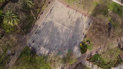 grupo de niños patinando en un parque de patinaje durante el día soleado rodeado de palmeras en buenos aires - toma aérea circular de arriba hacia abajo