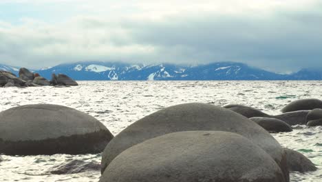 boulders sticking out of the water in lake tahoe, nevada with snow capped mountains in the background during a cloudy foggy day - sand harbor