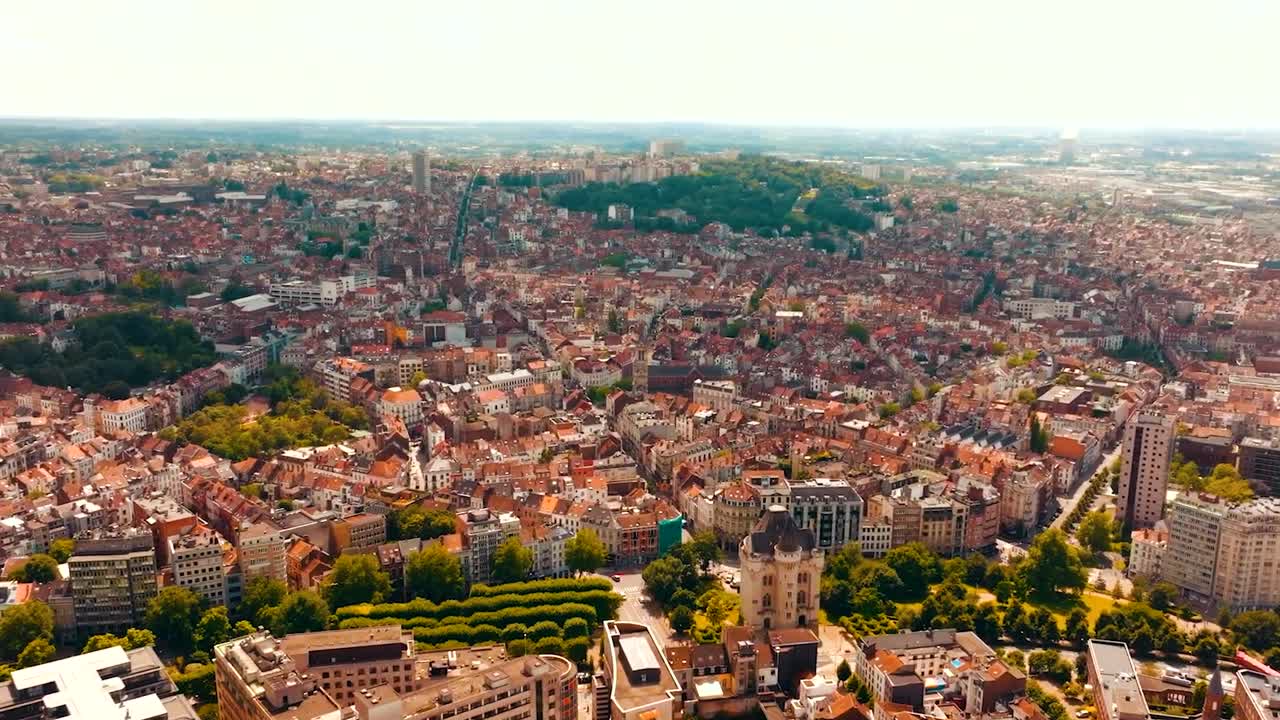Beautiful aerial drone footage flying over and panning over Brussels city in Belgium Europe during a sunny day with red rooftops, streets and horizon is visible in the background. Green trees visible.