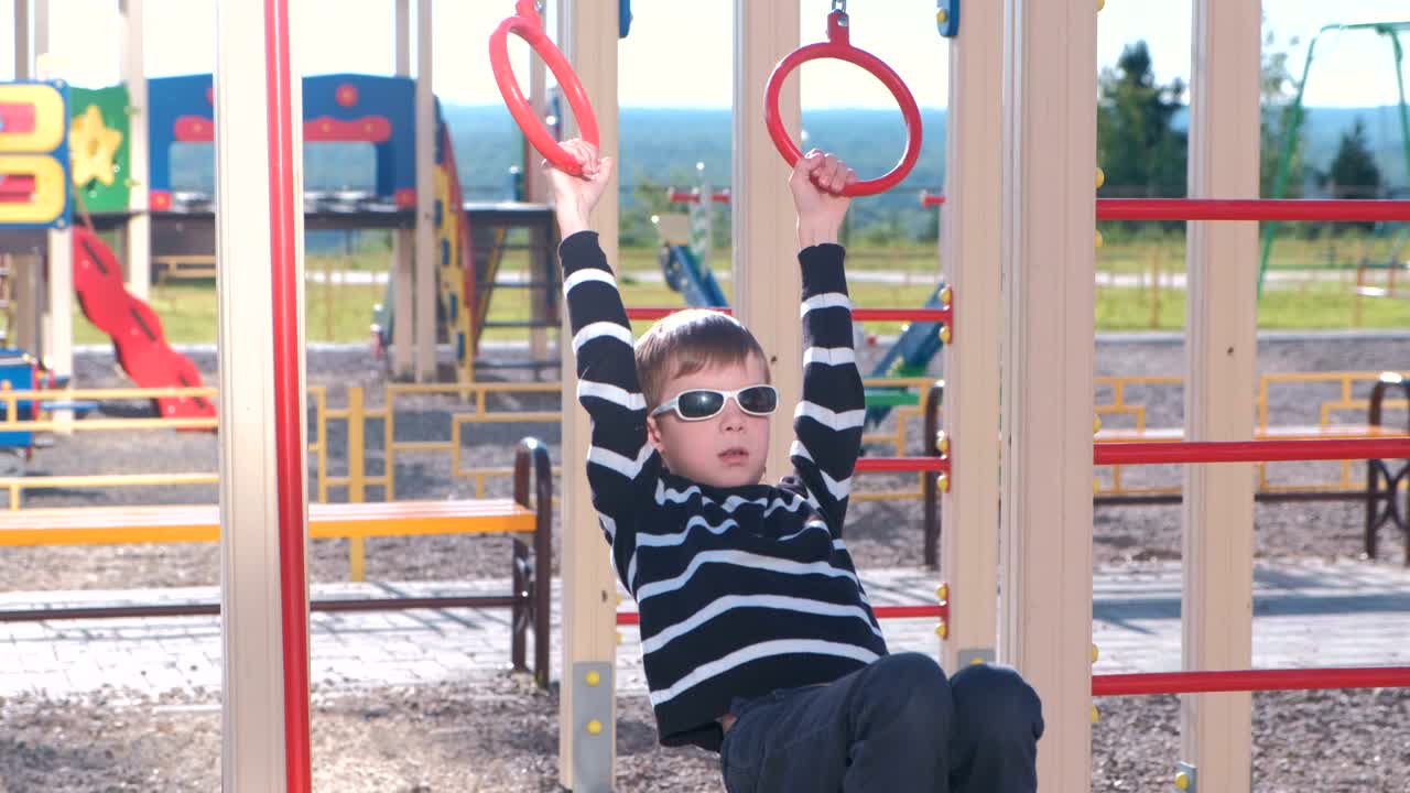 un niño de siete años cuelga de los anillos de gimnasia en el patio de recreo.