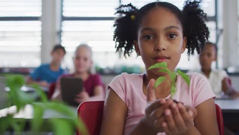 portrait of african american schoolgirl holding small plant, looking at camera