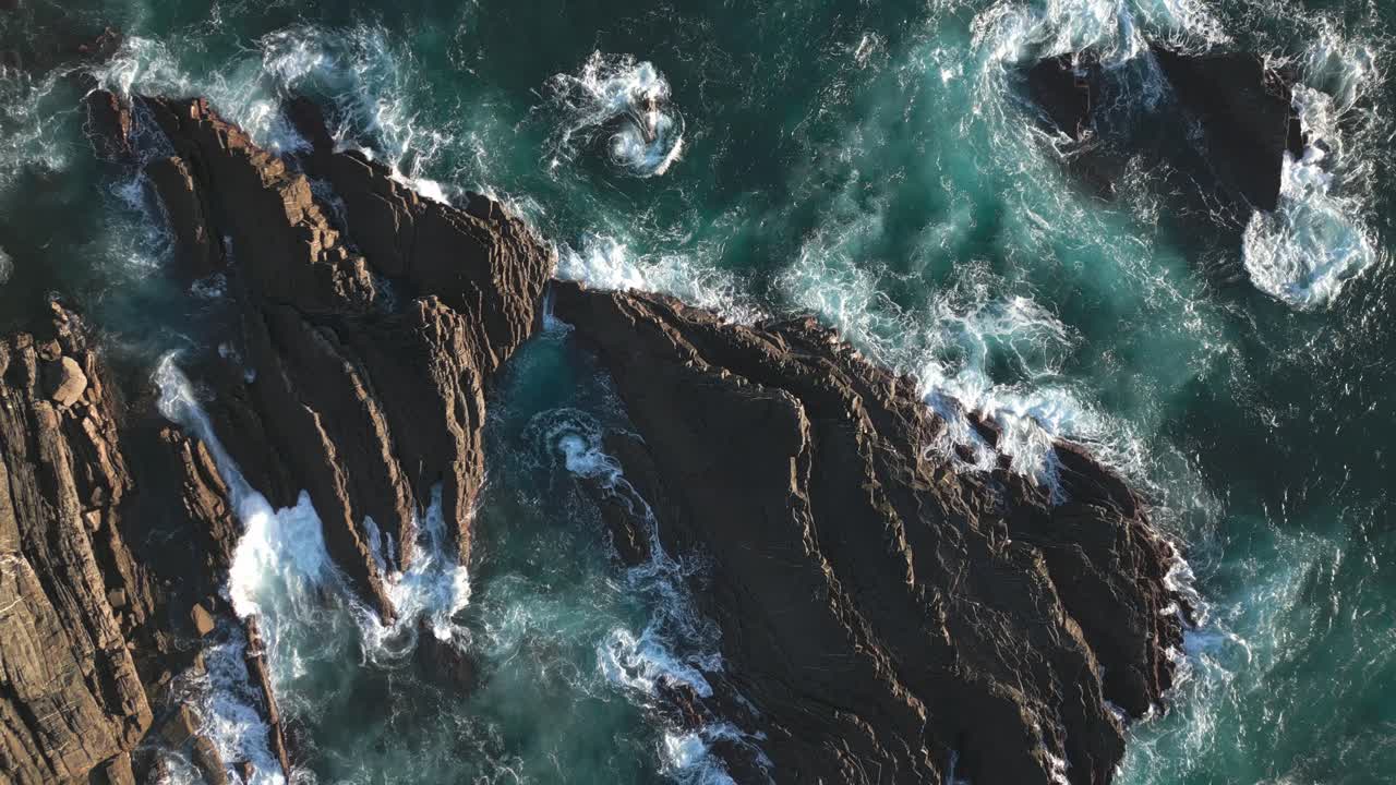 Rocky coast and rough sea water, ocean waves, aerial drone top down zoom out view
