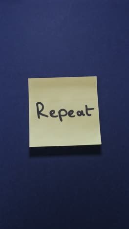posting repeat sticky note on dark blue wall, emphasizing consistency and routine