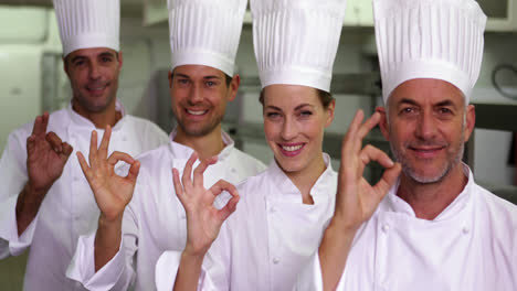 four cheerful chefs looking at camera making ok sign