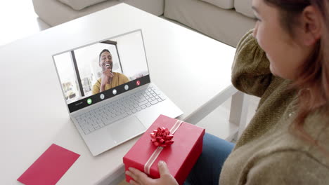 Caucasian-woman-holding-red-gift-using-laptop-with-african-american-man-on-screen