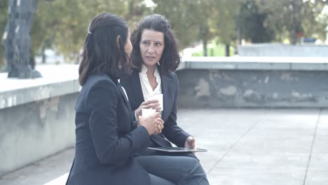 Brunette-partners-sitting-outside,-drinking-coffee-and-talking