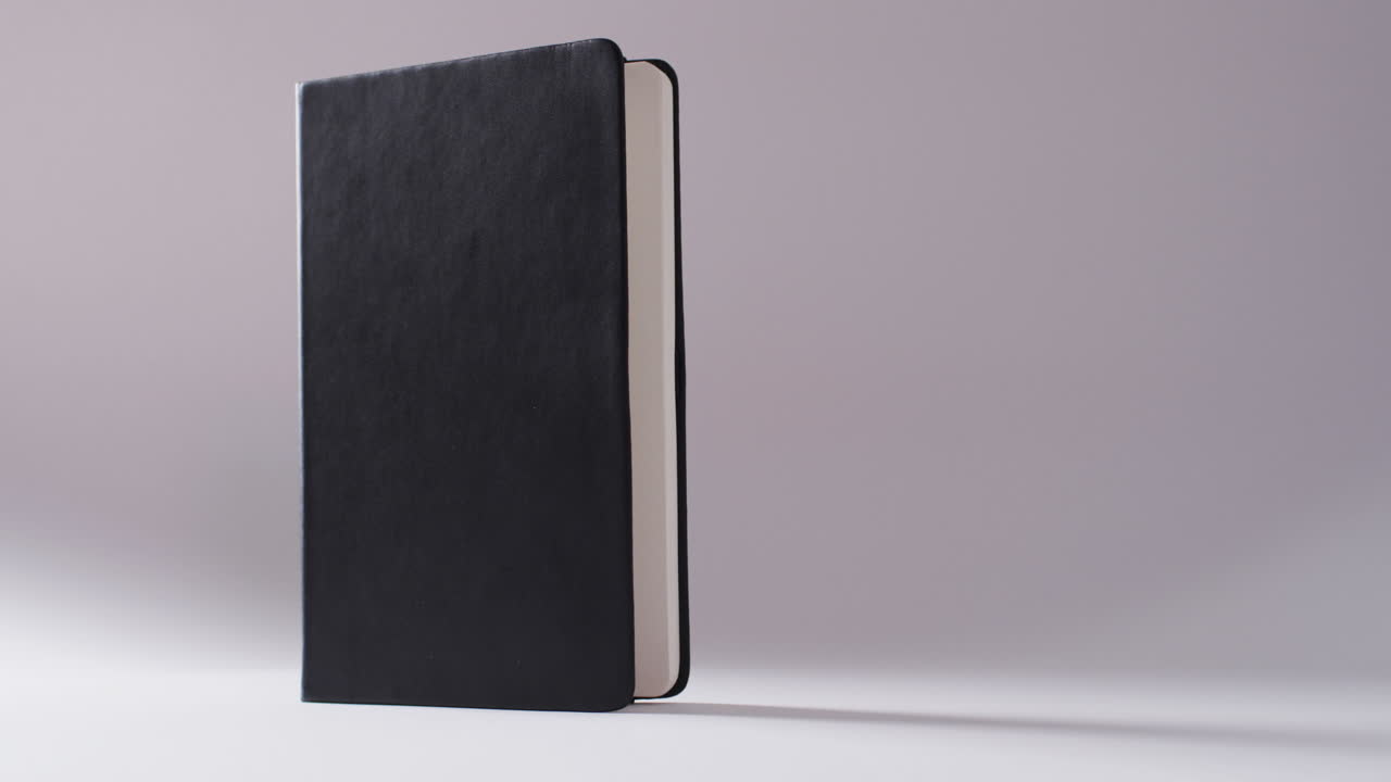 Close up of open black book standing vertical with copy space on white background in slow motion