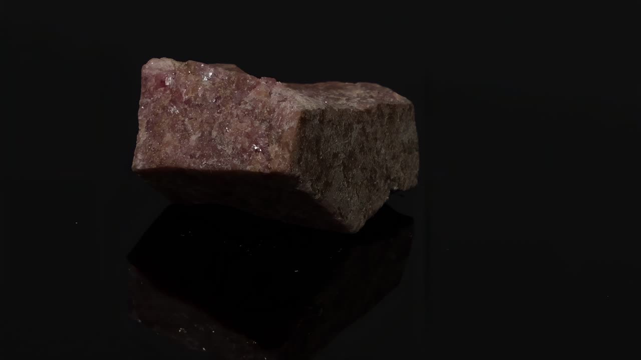 A portion of a pink mineral rotates, showcasing its texture and form against a black background.